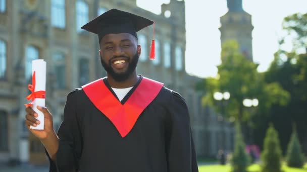 Eccitato afro-americano studente in abito di laurea in possesso di diploma alla ricerca della fotocamera — Video Stock