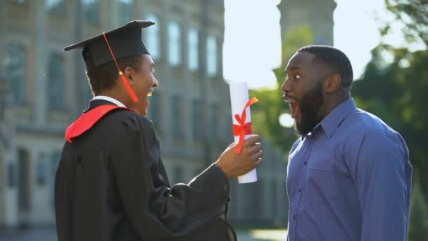 Papá emocionado e hijo graduado abrazándose al aire libre, logro de estudio, educación — Vídeo de stock