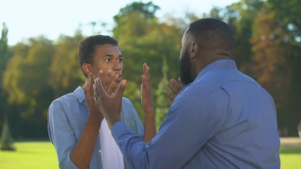 Американский отец и сын-подросток спорят на открытом воздухе, семейный конфликт, общение — стоковое видео