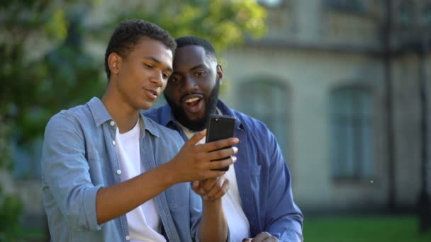 Happy male teenager showing smartphone application to father sitting outdoors — Stock Video