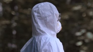 Koruyucu giysili biri şişeyi eziyor, plastik kirliliğinin farkında.