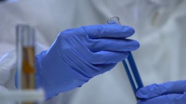 Koruyucu eldivenler içinde elinde biyolojik tehlikeli mavi sıvıyla deney tüpü tutan biri.