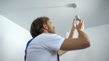 Professional electrician twisting bulb installing light in apartment, service