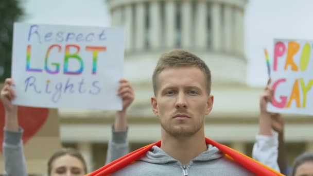 Молодой человек, поднимающий радужный флаг, участник ЛГБТ-митинга, марш гордости — стоковое видео