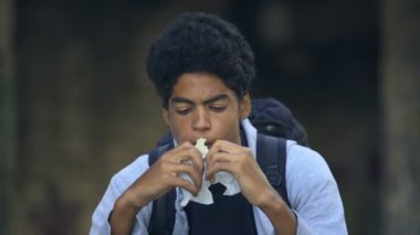Aç Afrikalı erkek tek başına oturmuş sandviç çiğniyor, depresyonda.