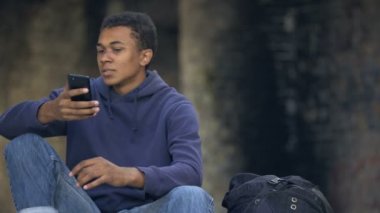 Afrikalı genç sinirli görünüyor akıllı telefon mesajı okuyor, ailevi sorunlar yaşıyor.