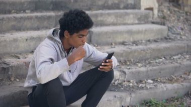 Depresif siyahi üniversite öğrencisi akıllı telefon müziği dinliyor, duygusal izolasyon