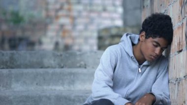 Depresyondaki genç erkek tuğla duvara yaslanıyor merdivenlerde oturuyor, aile içi şiddet
