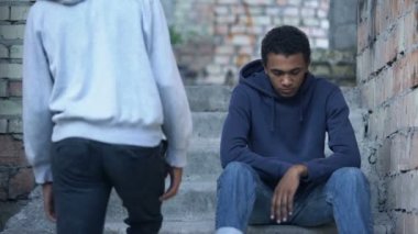 Genç adam üzgün arkadaşlarına elini uzatıyor merdivenlerde oturuyor, arkadaşlık desteği...