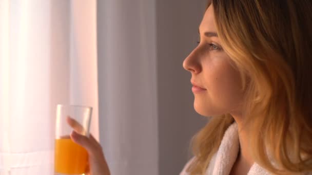 Žena pije pomerančový džus, dívá se do okna, ráno bere antioxidanty — Stock video