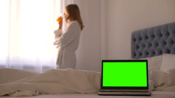 Ordinateur portable sur le lit, femme boire du jus de détente près de la fenêtre, réservation de voyage en ligne — Video