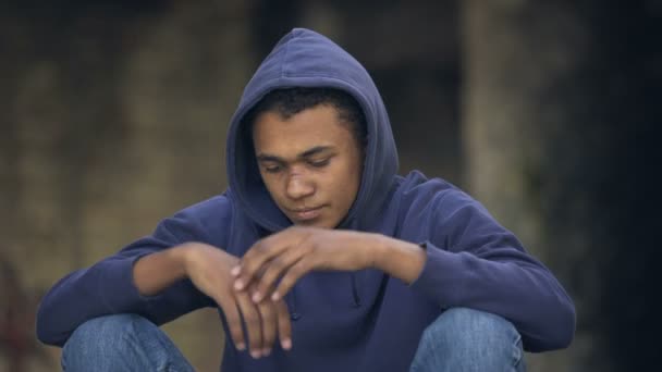 Отчаянный молодой человек сидит на улице в одиночестве, домашнее насилие, убегает из дома — стоковое видео