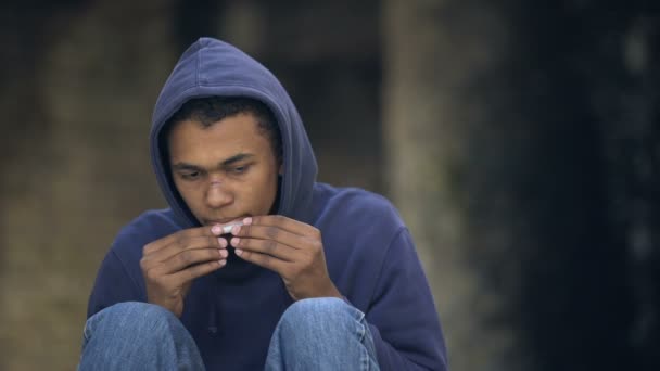 Man adolescent hoodie rollen en roken gezamenlijke, schadelijke nicotine puff, gevaar — Stockvideo