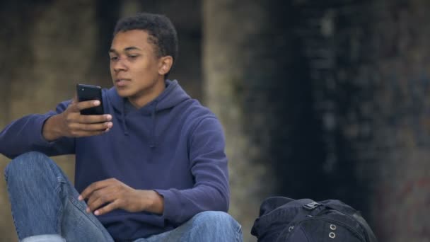 Afrikanischer Teenager sieht wütend aus, wenn er Smartphone-Nachrichten liest, Familienkrise — Stockvideo