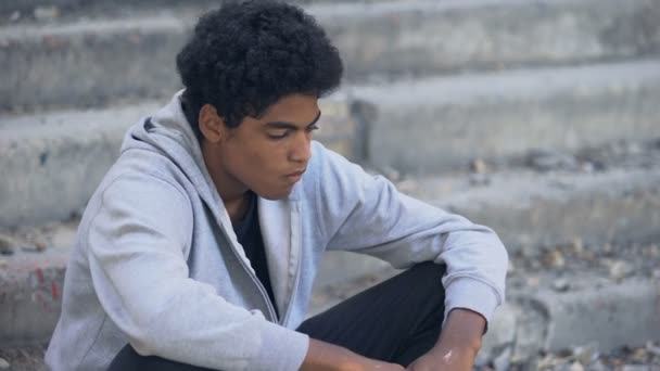 Sad male teenager putting on hood sitting city stairs alone, running from home — Stock Video