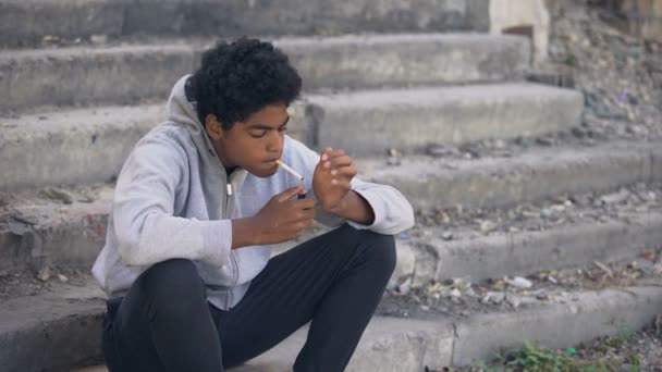 Unhappy african teenager smoking cigarette stairs, harmful puberty addiction — Stock Video
