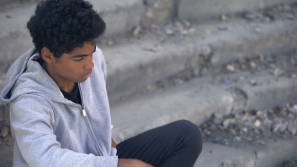 Sad poor teenager looking at coins in hand sitting outdoors, urban unemployment — Stock Video