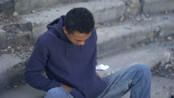 Poor young man counting money sitting alone city stairs, low living standard — Stock Video