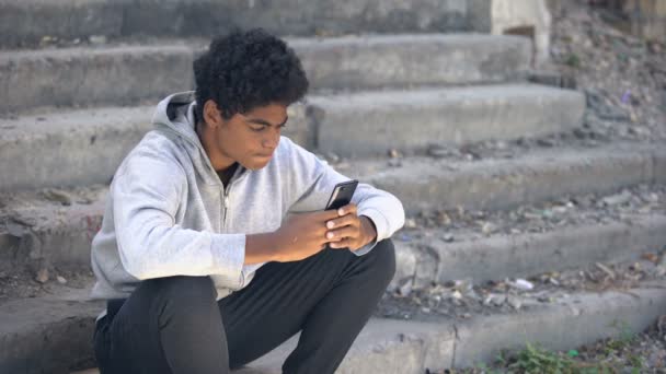 Подросток злится, читая сообщение на смартфоне, сидя на лестнице, проблемы полового созревания — стоковое видео