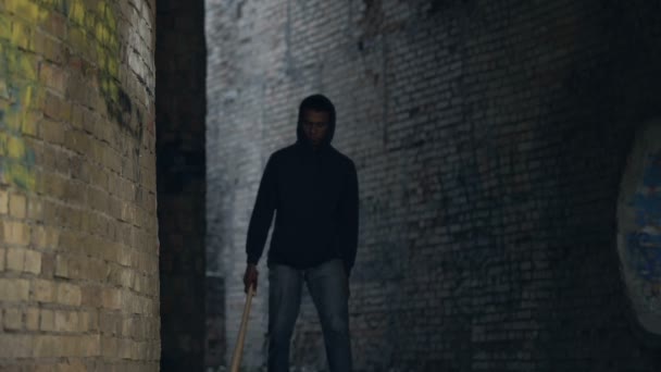 Adolescente negro caminando área abandonada de la ciudad con bate de béisbol, peligro de la ciudad — Vídeo de stock