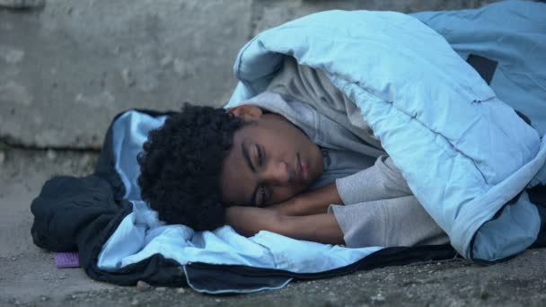 Homeless african teenager lying in sleeping bag ground, poverty unemployment — Stock Video