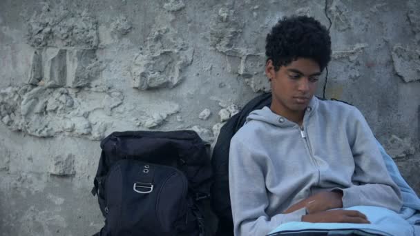 Sin hogar macho adolescente cubierta con durmiendo bolsa sentado calle cerca mochila — Vídeos de Stock