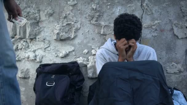 Hombre sin hogar llorando sentado en la calle, transeúnte donando dinero a pobre mendigo — Vídeo de stock