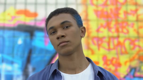 Cool male teenager with colored hair looking camera on graffiti wall background — Stock Video