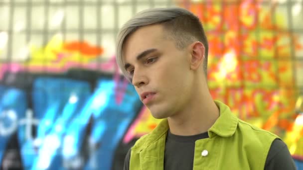 Adolescente masculino com cabelos coloridos posando no fundo do edifício graffiti, moda — Vídeo de Stock