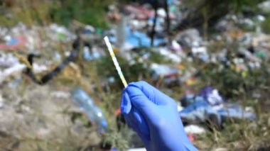 PH test şeridini atık depolama arkaplanı ve kirlilik seviyesine karşı tutan eldiven