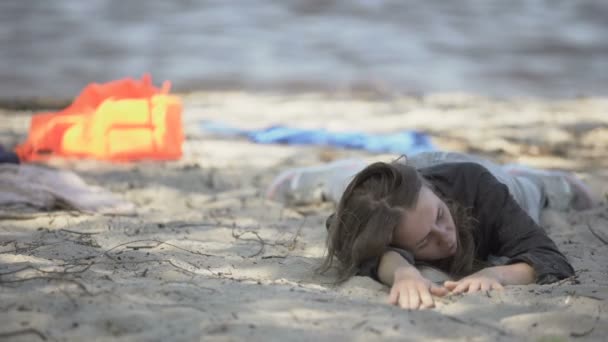 Wyczerpana kobieta leżąca na plaży, szukająca pomocy, ocalała z katastrofy — Wideo stockowe