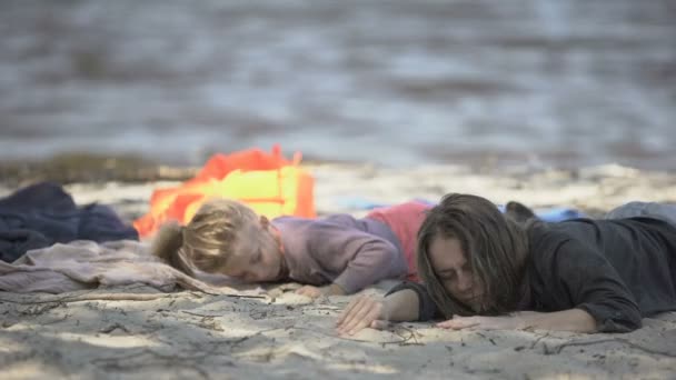 Mother and daughter lying on seashore, feeling unwell after shipwreck, survivors — ストック動画