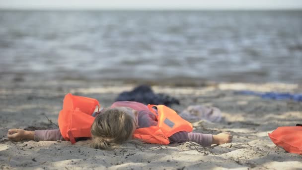 Bambina in giubbotto di salvataggio sdraiata sulla riva del mare, sopravvissuta all'alluvione naturale — Video Stock