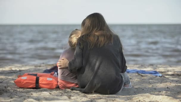 Madre e hija sentadas cerca de los chalecos salvavidas en la orilla del mar, sobrevivieron al desastre — Vídeo de stock