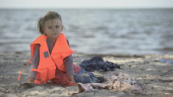 Rifugiato bambino solitario in giubbotto di salvataggio seduto sulla riva, migrazione pericolosa attraverso il mare — Video Stock