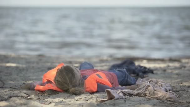 Little girl wearing life jacket lying on shore, survived plane crash, disaster — Stock Video