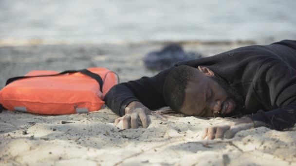 Afro-Amerikalı adam kıyıda acı çekerek yatıyor. Mülteciler gemi enkazından kurtuldu. — Stok video
