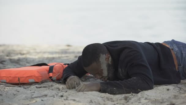 Distressed man suffering pain lying near lifejacket, asking help after shipwreck — Stock Video