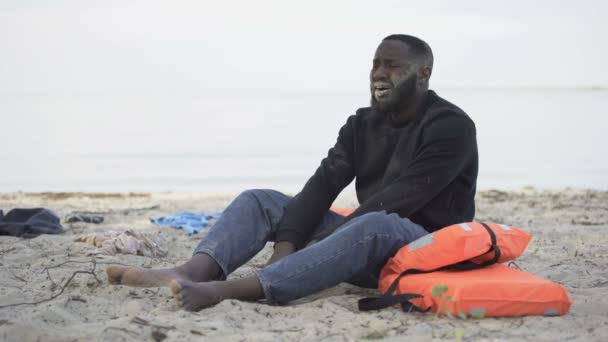 Wanhopige zwarte man huilend aan wal, vluchteling overleefde schipbreuk, verloren huis — Stockvideo