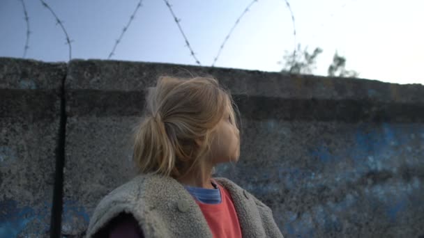 Little girl with muddy face standing at barbed wire, war child in refugee camp — Stock Video