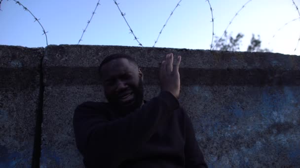 Hombre negro deprimido escondiendo la cara en remordimiento llorando cerca de alambre de púas, campo de refugiados — Vídeos de Stock