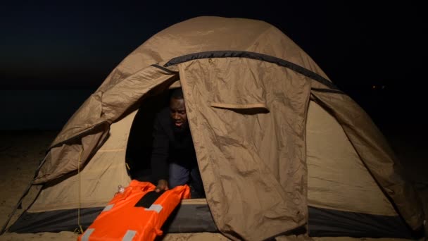 Беженец войны, обнимающий спасательный жилет в палатке, подавленный постоянным чувством опасности — стоковое видео