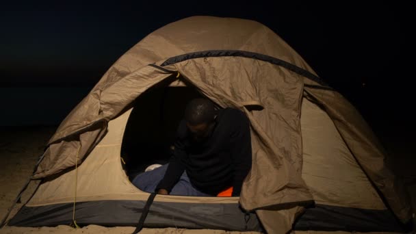 Несчастный черный мужчина плачет в палатке, бездомный беженец болен и голоден в лагере — стоковое видео