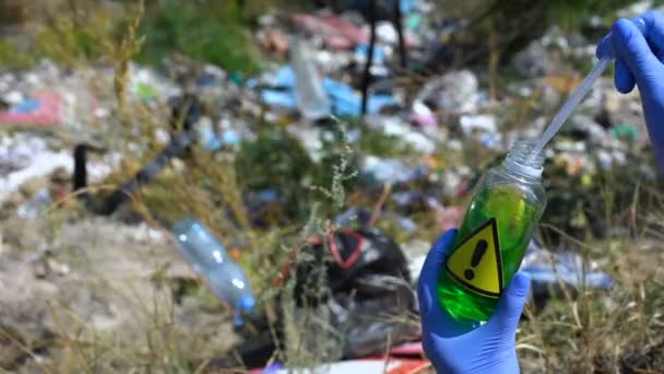 廃棄物の背景に警告標識付きボトルからサンプルを取る生態学者 — ストック動画