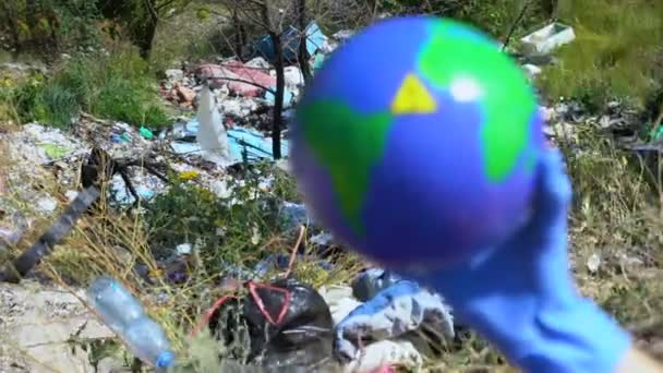 Persona che detiene il globo terrestre con un segnale di avvertimento sullo sfondo di dumping aperto — Video Stock