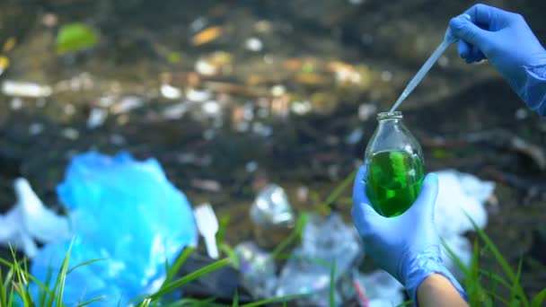 Ökologe in Handschuhen entnimmt vor verschmutztem See Probe aus Flasche — Stockvideo