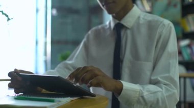 Okul üniformalı genç bir erkek internette tablet üzerinde ödev yapıyor, uzaktan çalışıyor.