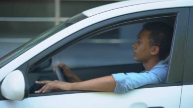 Trafik sıkışıklığında sıkışmış, direksiyona yaslanmış yorgun, melez bir genç.