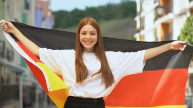 Almanya 'nın bayrağını sallayan neşeli genç ve kameraya gülümseyen, ulusal bayram