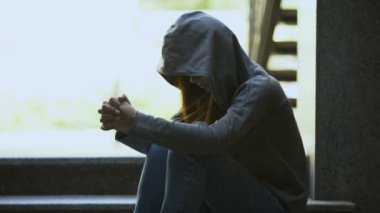 Kapüşonlu, depresyondaki genç bir kadın merdivenlerde tek başına oturmuş sorunları düşünüyor.